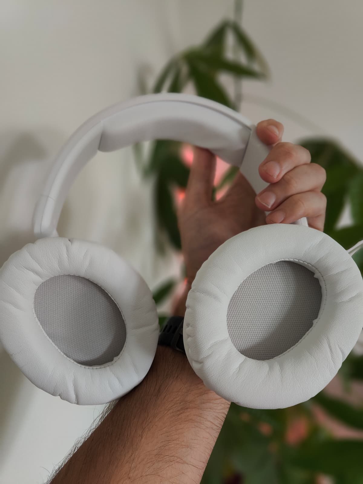 Twee handen houden de HyperX Cloud Flight 2 omhoog, met zicht op de dikke witte oorkussens